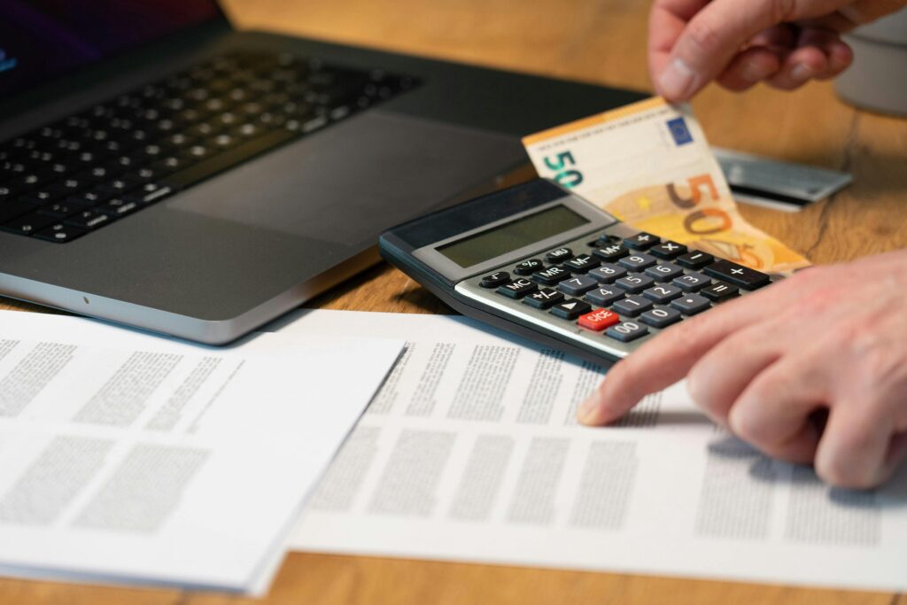 Close-up of hands using calculator with euro notes and laptop on desk.